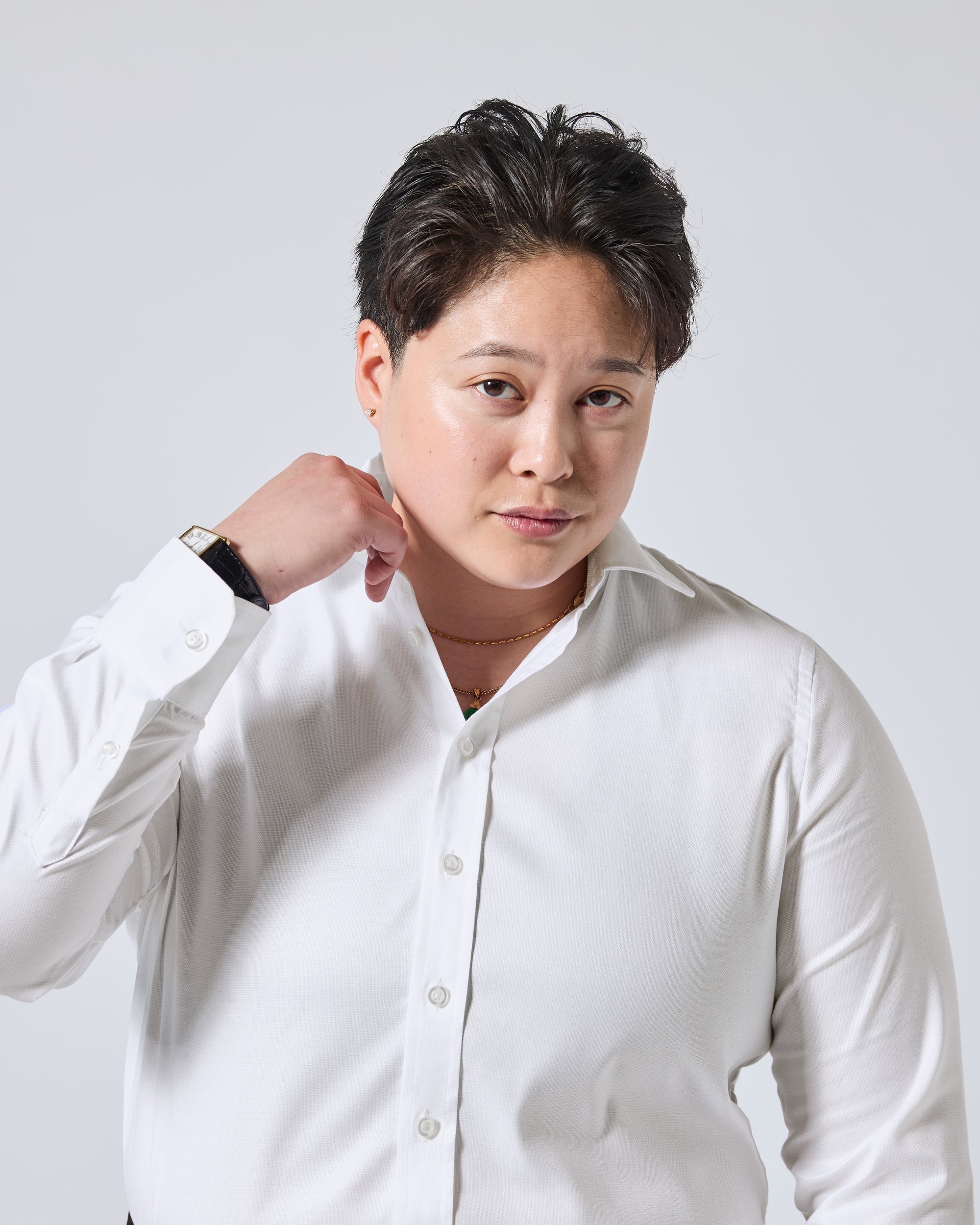 Model wearing a white long-sleeve button-up shirt, standing against a light gray background with one hand by their neck. Color: White