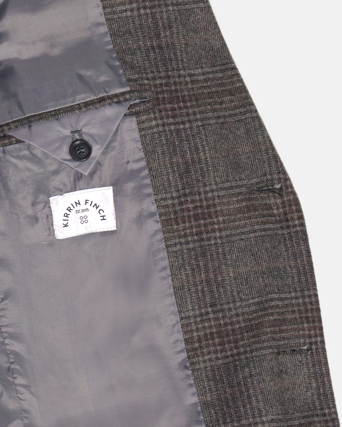 Close-up detail of a tailored jacket or vest showing the textured plaid wool fabric, a black button, and a white interior label. Color: Earthen Glen Plaid