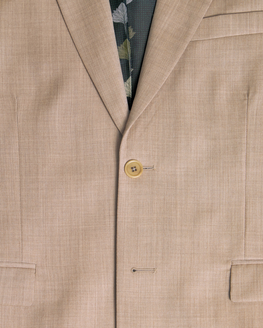 Close-up of a beige suit jacket with a button and floral patterned inner lining. Color: Desert