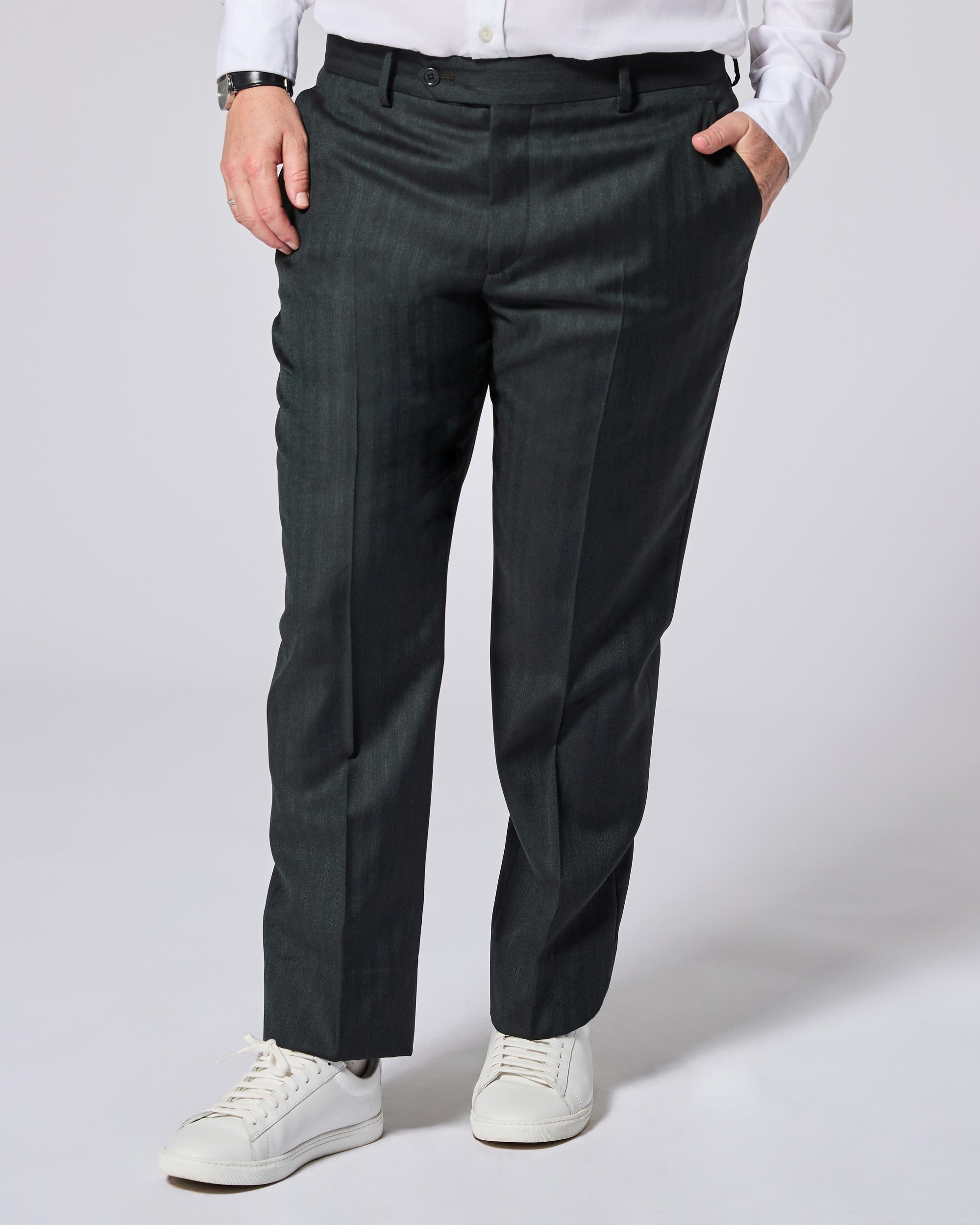 A person wearing dark green pinstriped trousers, styled with a white shirt and white sneakers, shown from the waist down on a light gray studio background. Color: Midnight Pine Herringbone