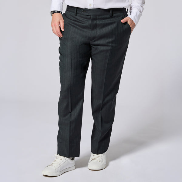 A person wearing dark green pinstriped trousers, styled with a white shirt and white sneakers, shown from the waist down on a light gray studio background. Color: Midnight Pine Herringbone
