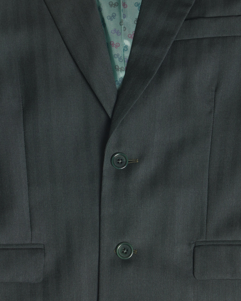 Close-up of a dark green suit jacket with two buttons, showing a patterned teal inner lining. Color: Midnight Pine Herringbone