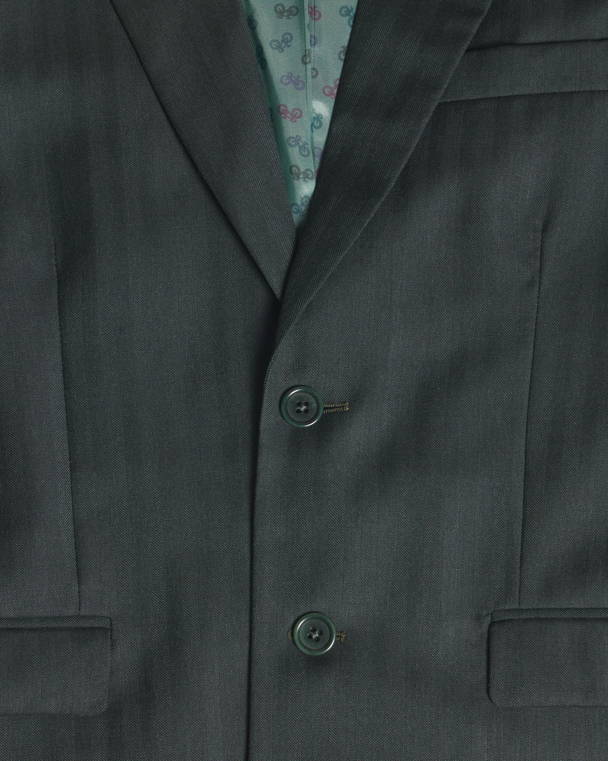 Close-up of a dark green suit jacket with two buttons, showing a patterned teal inner lining. Color: Midnight Pine Herringbone