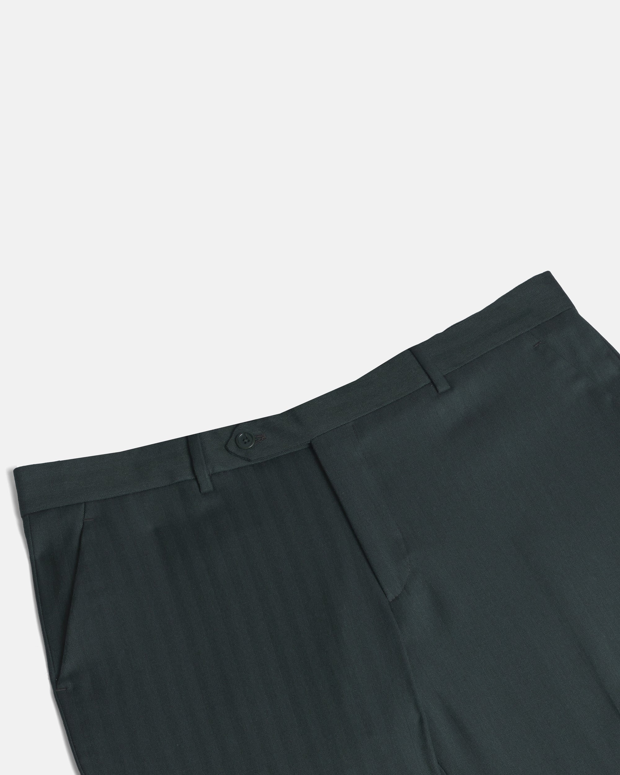 Close-up of dark green pinstriped trousers showing the waistband, button closure, belt loops, and front pleat detail against a light gray background. Color: Midnight Pine Herringbone