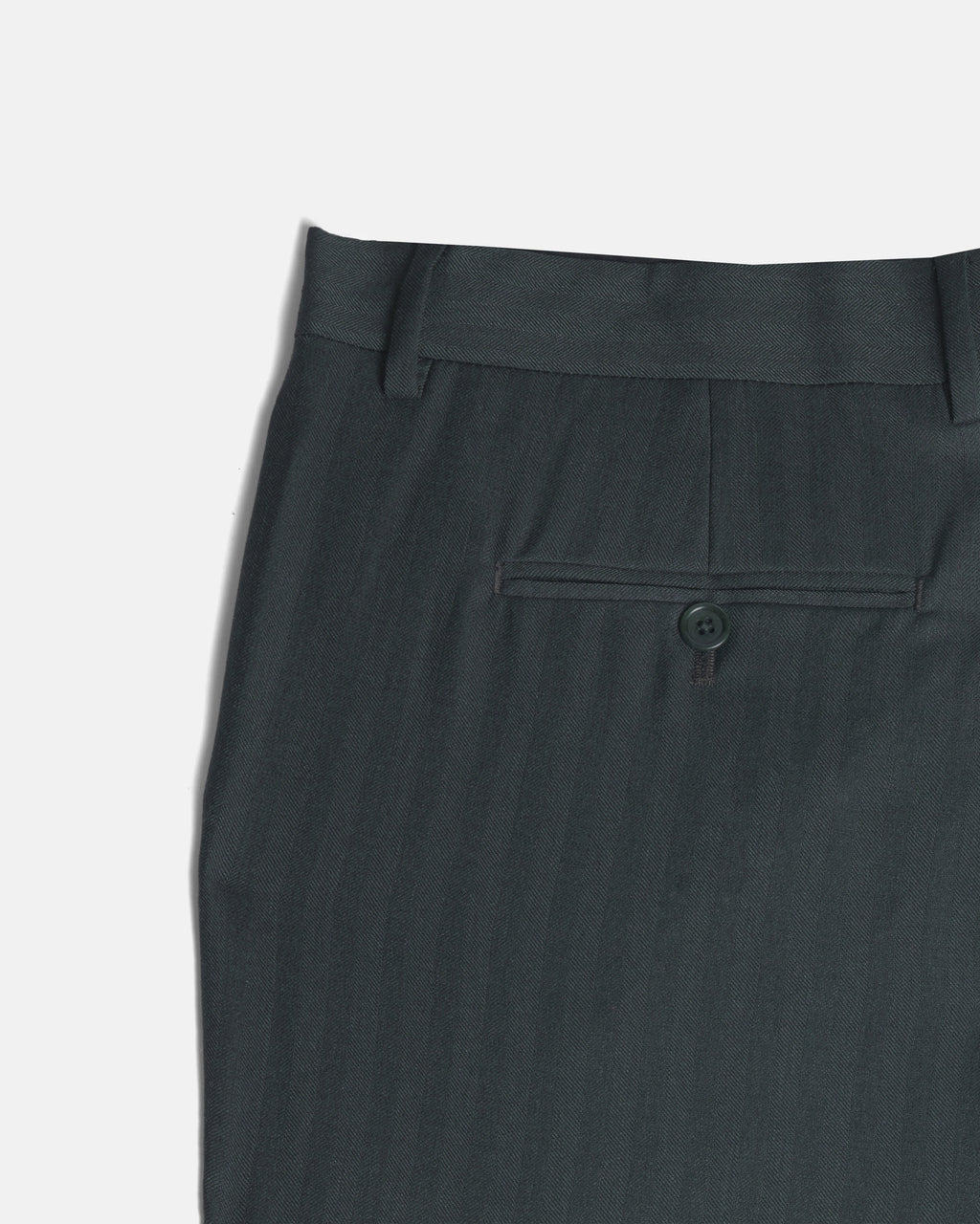 Close-up of the waistband and back pocket of dark green trousers, showing a buttoned welt pocket and belt loops against a light gray background. Color: Midnight Pine Herringbone