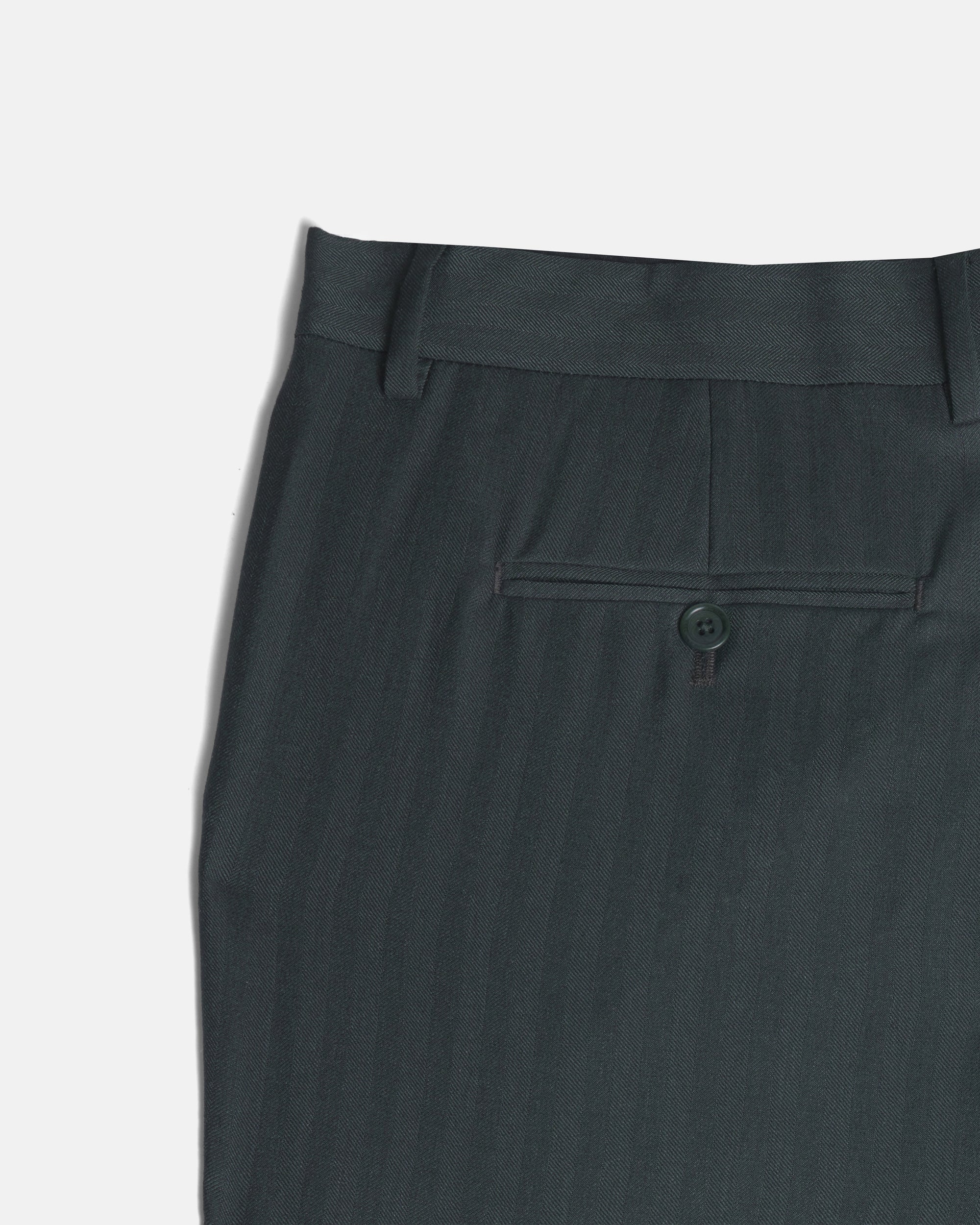Close-up of the waistband and back pocket of dark green trousers, showing a buttoned welt pocket and belt loops against a light gray background. Color: Midnight Pine Herringbone
