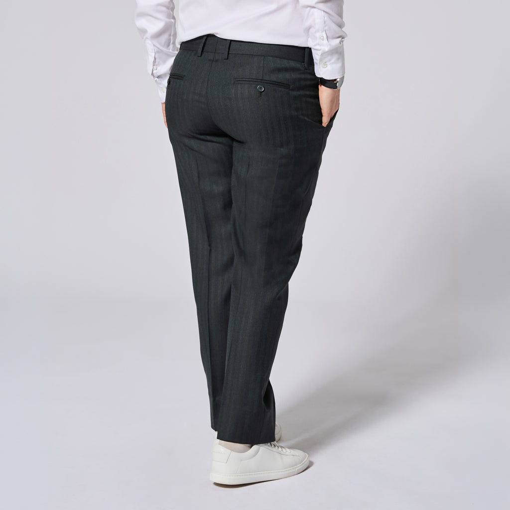 A person shown from the back wearing dark green pinstripe trousers, a white long-sleeve shirt, and white sneakers against a light gray studio background. Color: Midnight Pine Herringbone