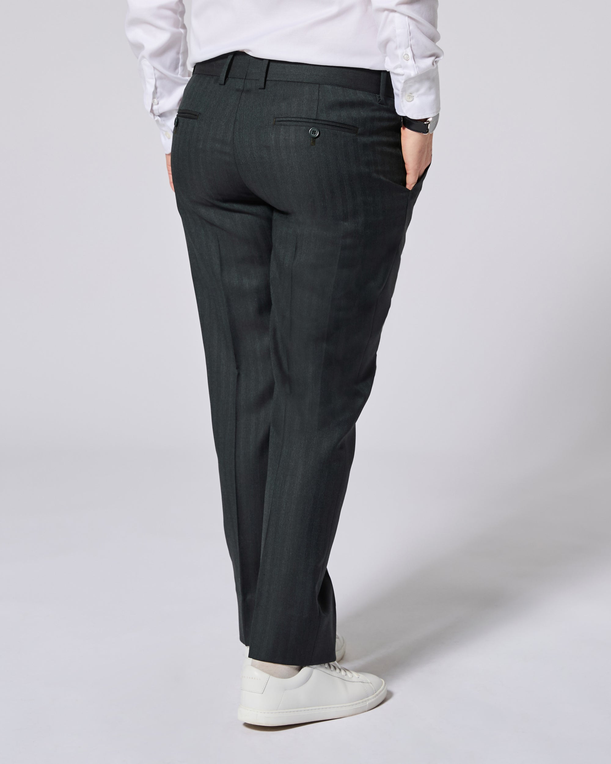 A person shown from the back wearing dark green pinstripe trousers, a white long-sleeve shirt, and white sneakers against a light gray studio background. Color: Midnight Pine Herringbone