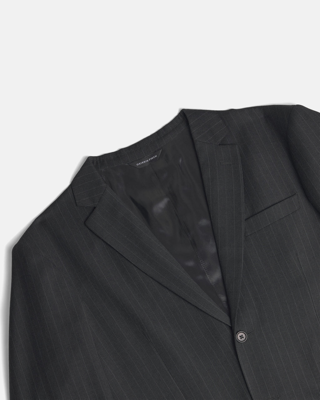 A close-up of a dark charcoal gray pinstripe suit jacket, showing the lapel, inner collar, and a single button closure against a light gray background. Color: Shadow Pinstripe