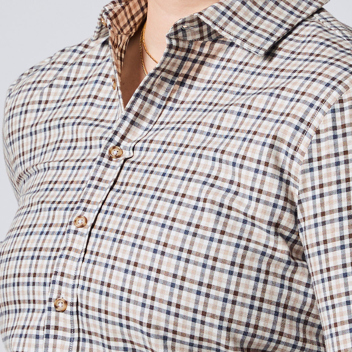 Close-up of a person wearing a beige plaid button-up shirt with brown and navy lines, gold buttons, and a gold necklace. Color: Herritage Plaid