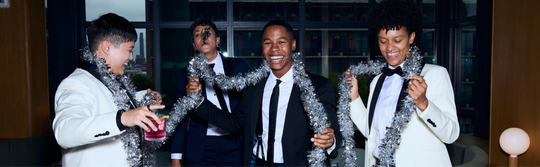 Four masc women in formal attire with tinsel around their necks, sitting together.