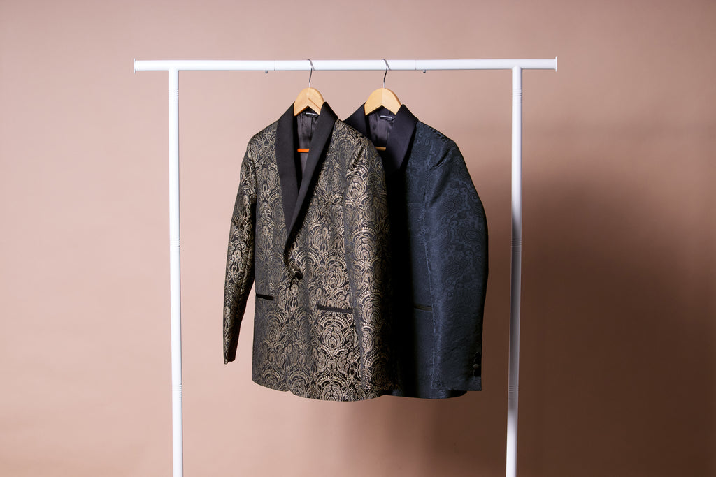 Two patterned blazers hanging on a rack against a beige background. Color: Gilded Brocade