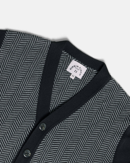Close-up of a knit cardigan with a dark navy V-neck and button placket, paired with a gray and black herringbone pattern on the body. Color: Inkstone Herringbone
