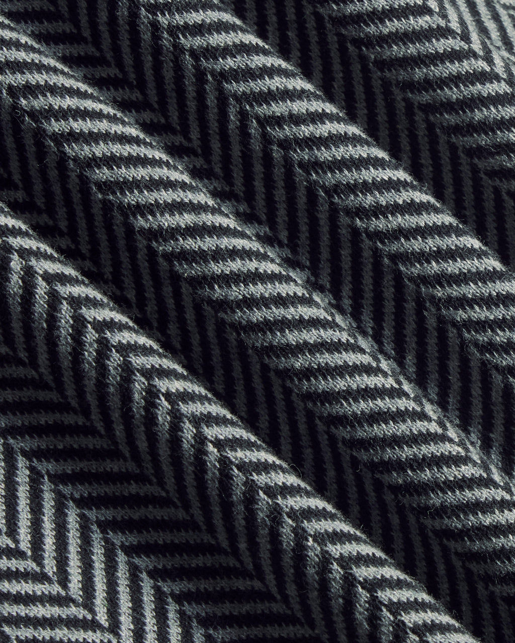 A close-up of a woven fabric with a dark gray and black herringbone pattern, showing the texture and diagonal folds. Color: Inkstone Herringbone