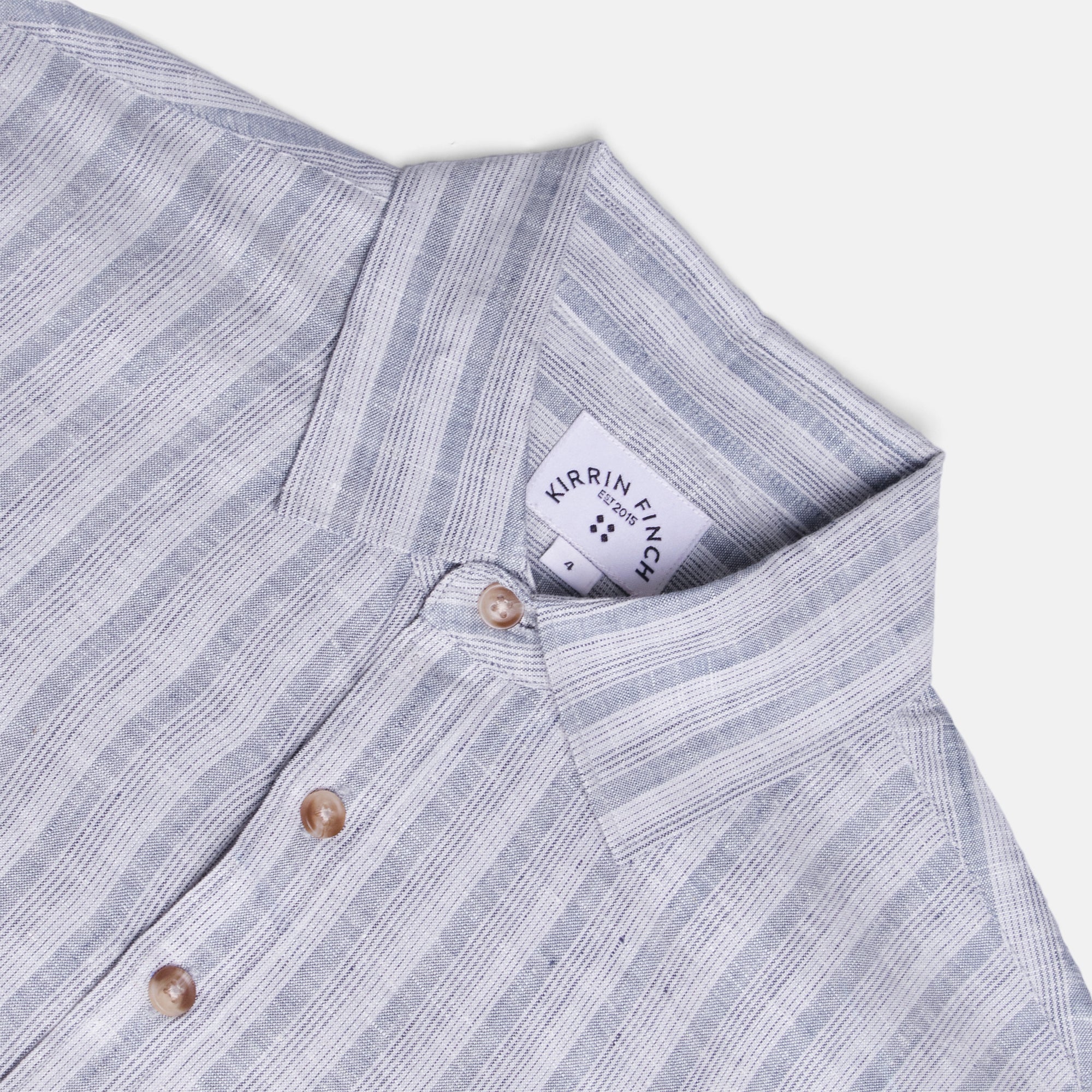 Close-up of a striped shirt with a Kirrin Finch label on a light gray background. Color: Coastal Blue