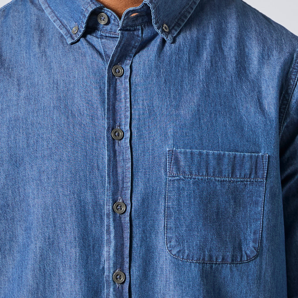 Close-up of a blue denim button-down shirt with a chest pocket, shown on a model. Color: Denim