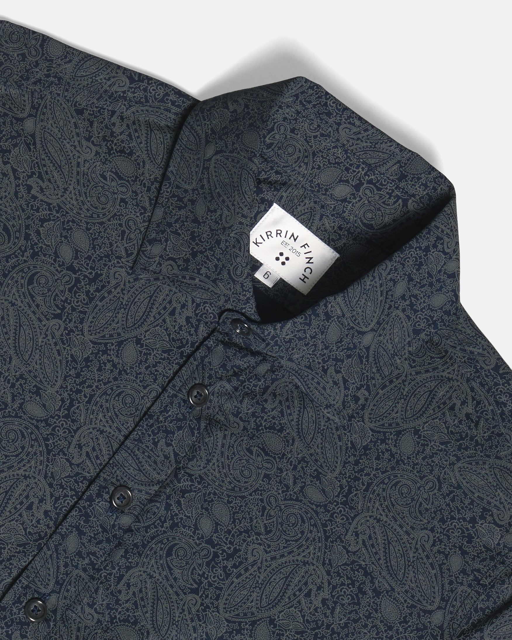 Close-up of a dark navy blue paisley patterned shirt, showing the collar, button placket, and inner brand label. Color: Midnight Paisley