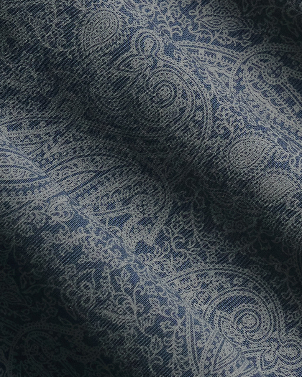 A close-up of a navy blue fabric with a detailed off-white paisley pattern, showing soft folds and shadows. Color: Midnight Paisley