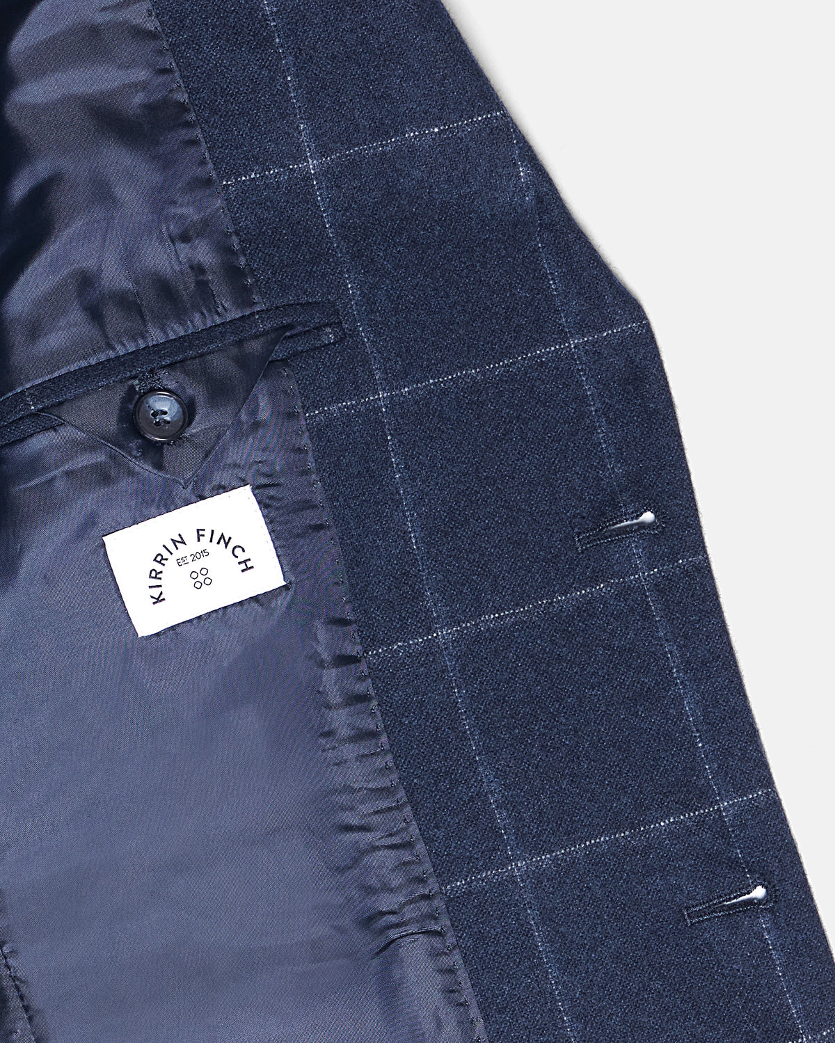 Close-up of a navy blue tailored blazer with a subtle windowpane check pattern, showing the dark navy lining, a buttoned pocket, and a white sewn-in label. Color: Navy Regatta
