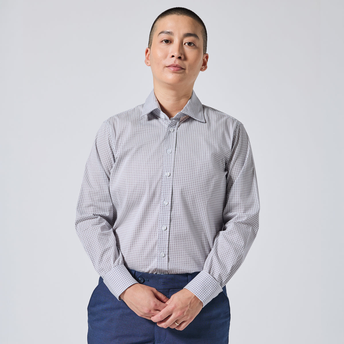 A person wearing a long-sleeve button-up shirt paired with navy blue trousers, standing against a light gray studio background. Color: Navy Rosette