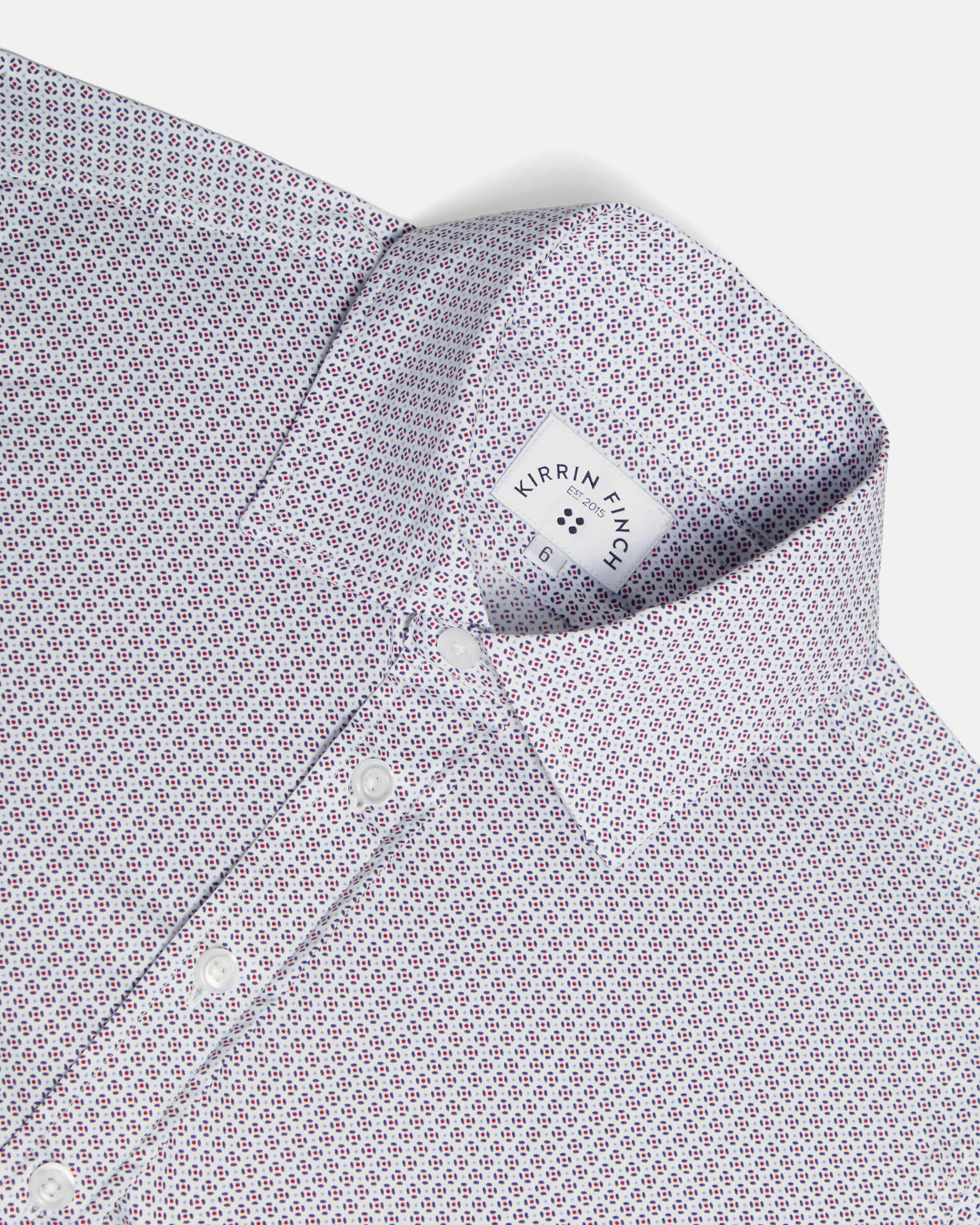 Close-up of a collared dress shirt with a small repeating geometric pattern in white, purple, and red, shown on a light gray background. Color: Navy Rosette