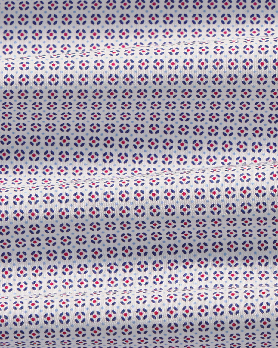 A close-up of a white fabric with a repeating geometric pattern of small red and blue diamond-like motifs. Color: Navy Rosette