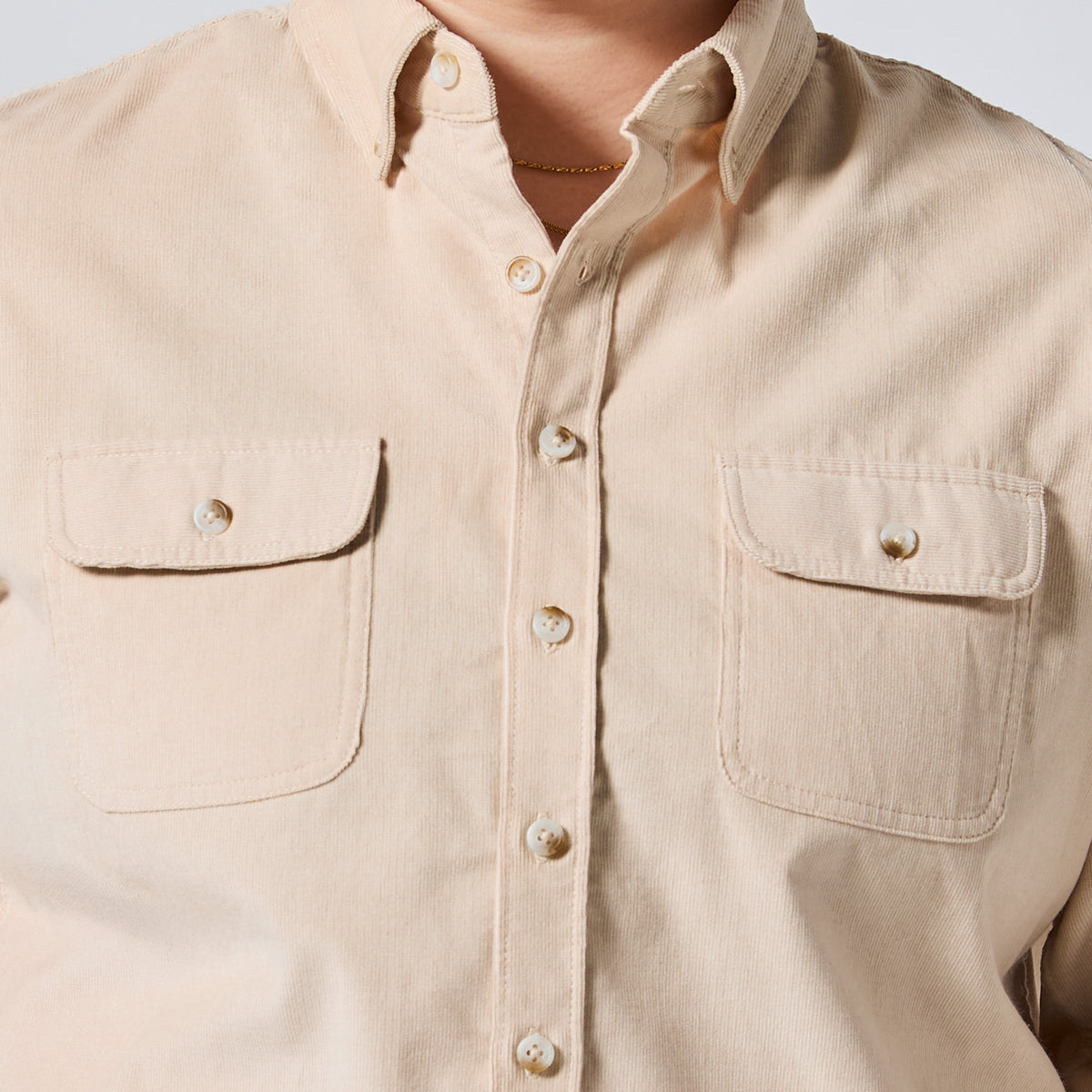 Close-up of a beige button-up shirt with two chest pockets and pearl-like buttons, worn by a model. Color: Oatmeal