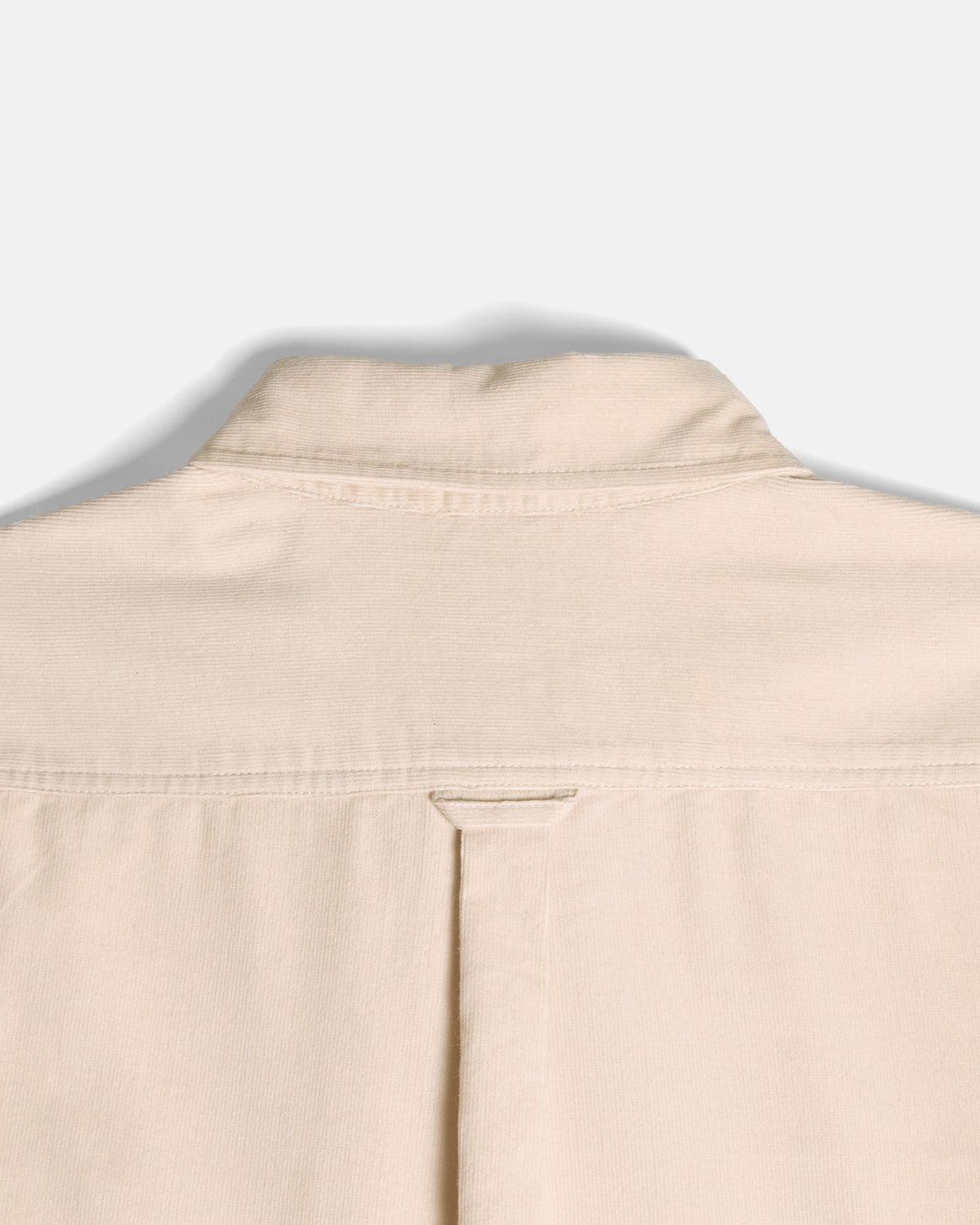 Close-up of the back collar and upper back of a light beige or cream-colored shirt, showing fabric texture and stitching against a plain light gray background.  Color: Oatmeal