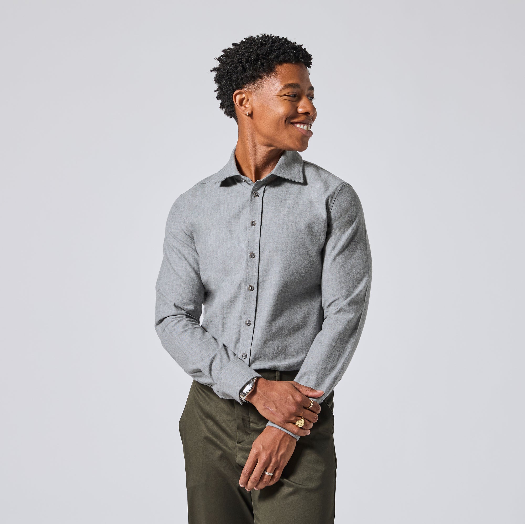 Model wearing a light gray long-sleeve button-down dress shirt and olive green trousers, standing against a light gray studio background. Color: Pewter Herringbone