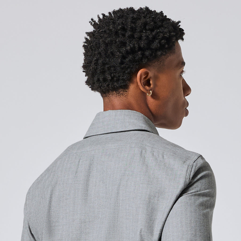 Model shown from the back and side profile wearing a light gray textured collared shirt or blazer against a plain light gray studio background. Color: Pewter Herringbone