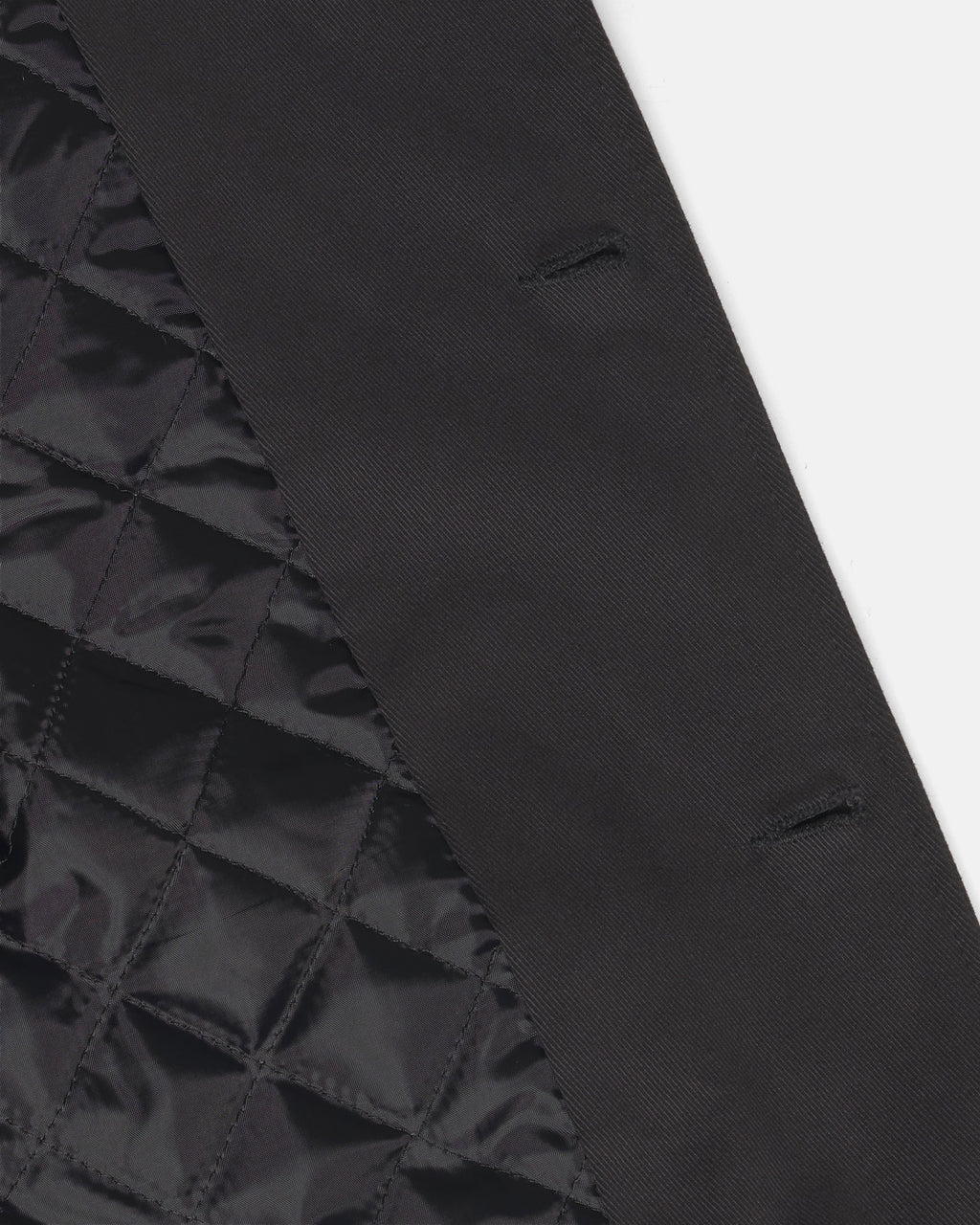 Close-up detail of a black quilted fabric panel meeting a smooth black woven fabric panel, showing texture and stitching on the Raven Quilted Jacket.