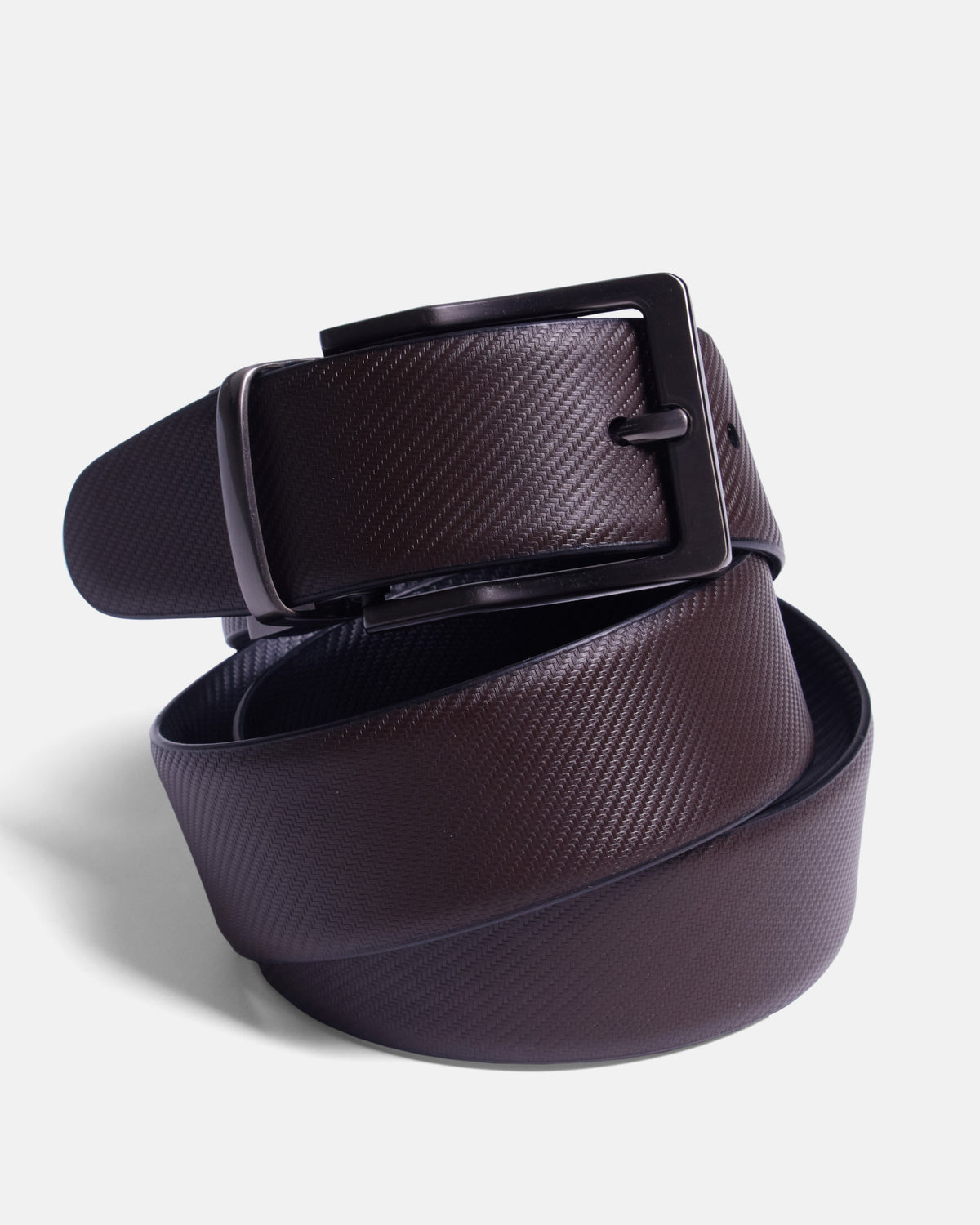 A dark brown textured leather belt with a matte black metal buckle, neatly coiled on a light gray background. Color: Black Twill/Brown Twill