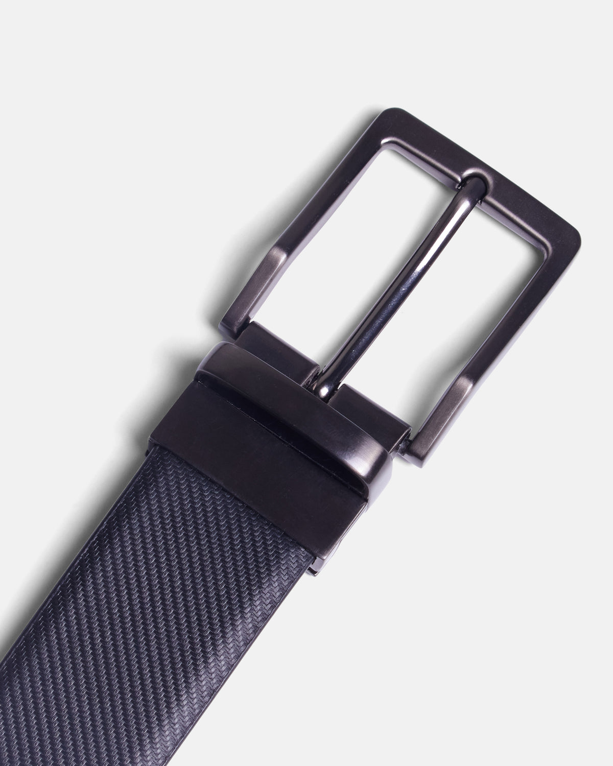 A close-up of a black textured strap with a polished dark gunmetal buckle, shown against a light gray background. Color: Black Twill/Brown Twill