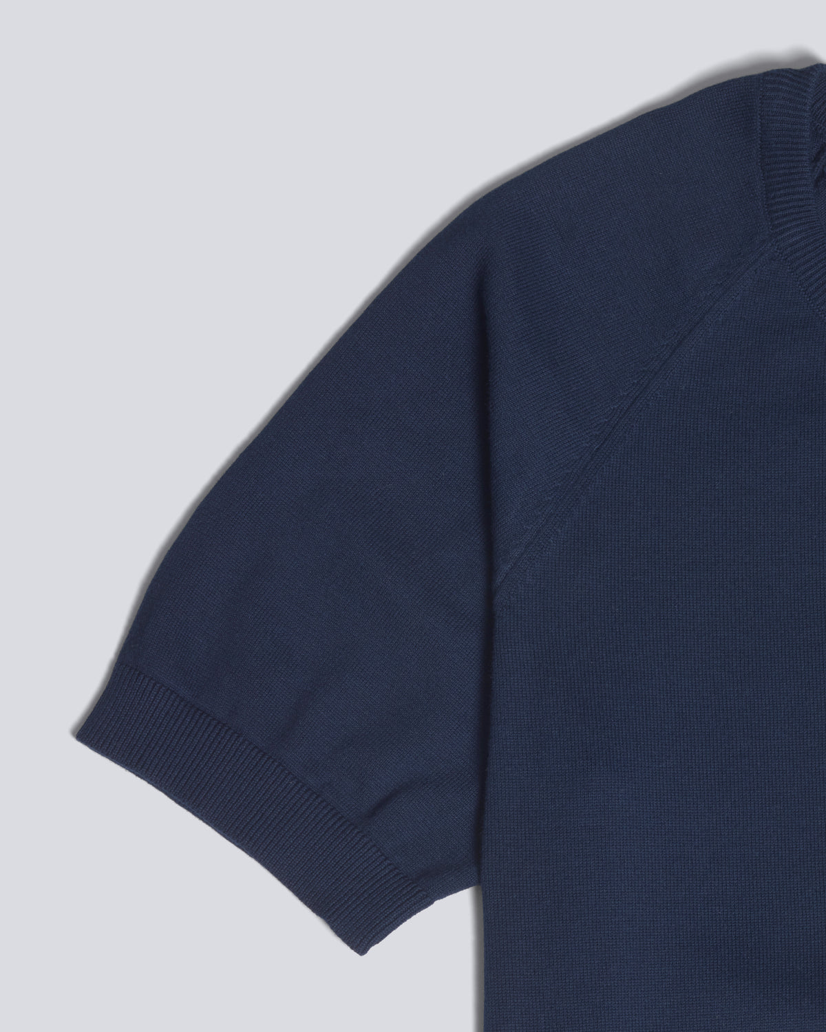 Close-up of a navy blue short-sleeve knit top showing the sleeve, ribbed cuff, and part of the shoulder against a light gray background. Color: Navy