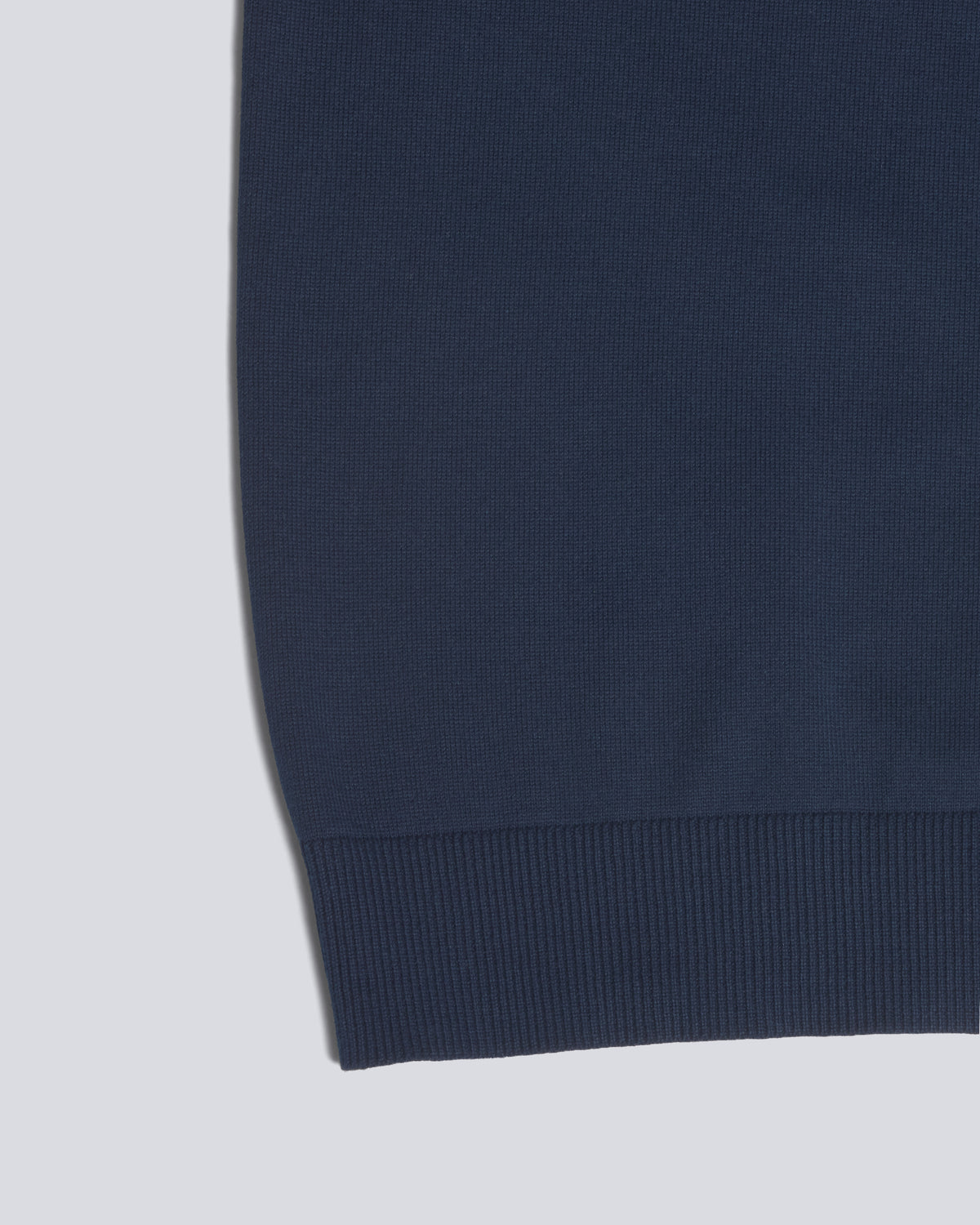 Close-up detail of a navy blue ribbed knit garment, showing the fabric texture and ribbed cuff against a light gray background. Color: Navy
