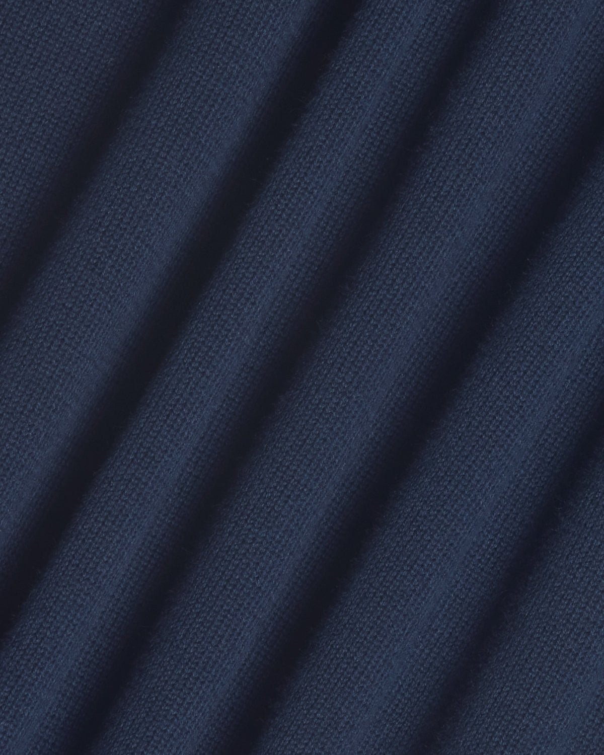 A close-up of dark navy blue knit fabric with diagonal folds showing the textured weave. Color: Navy