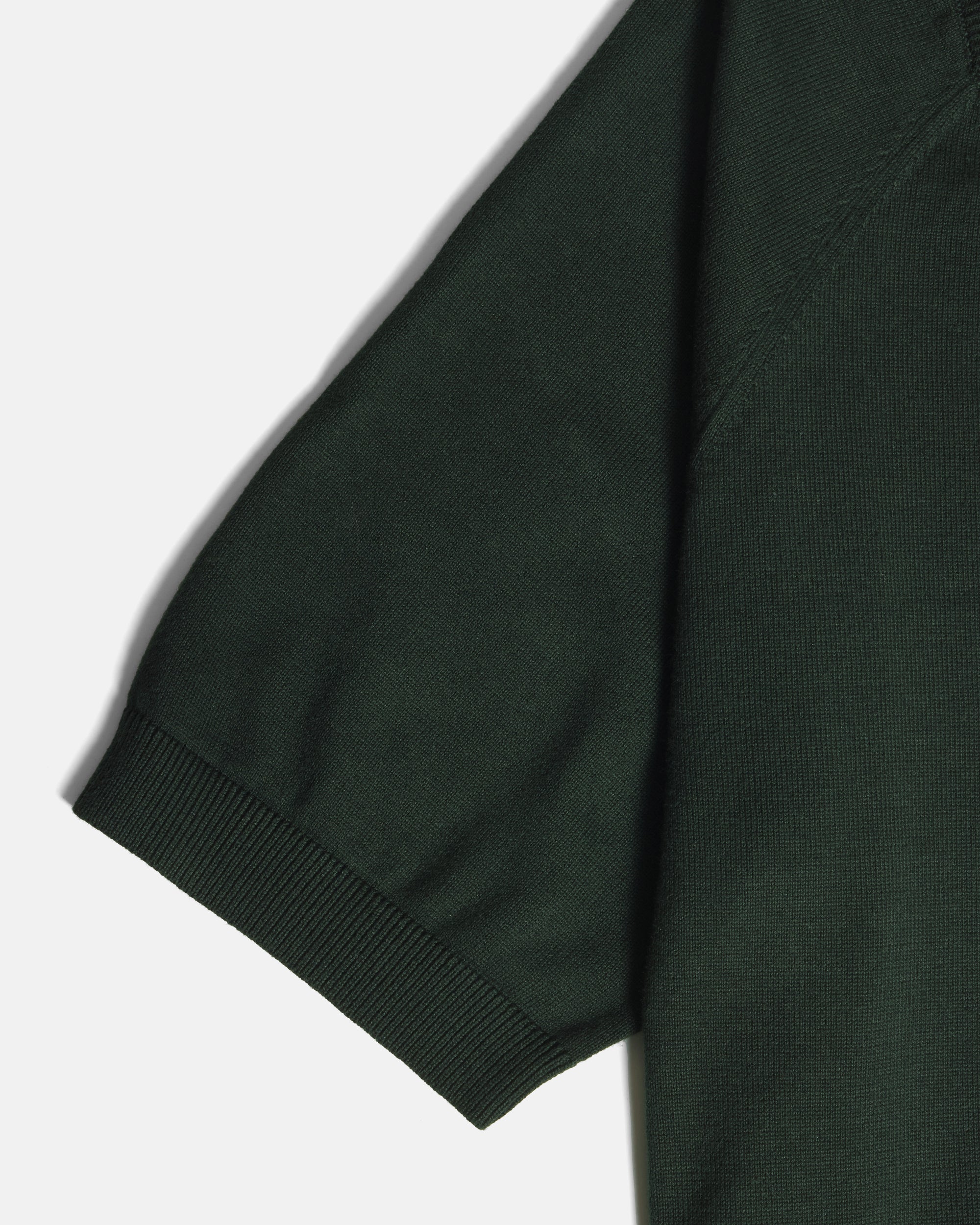 Close-up of a dark forest green short-sleeve knit garment, showing the ribbed cuff and part of the sleeve against a light gray background. Color: Evergreen