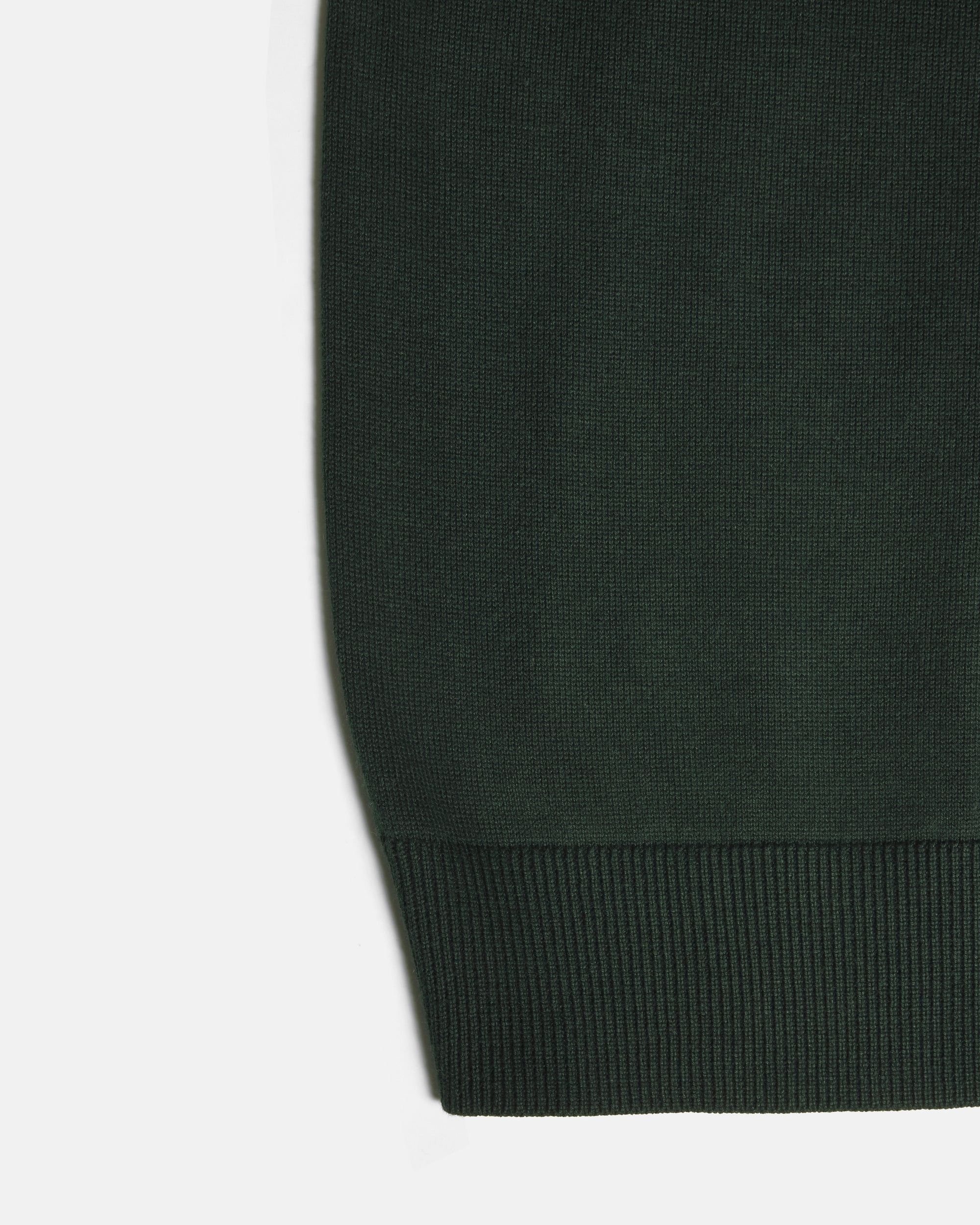 Close-up of a dark forest green knit fabric with a ribbed cuff on a white background. Color: Evergreen