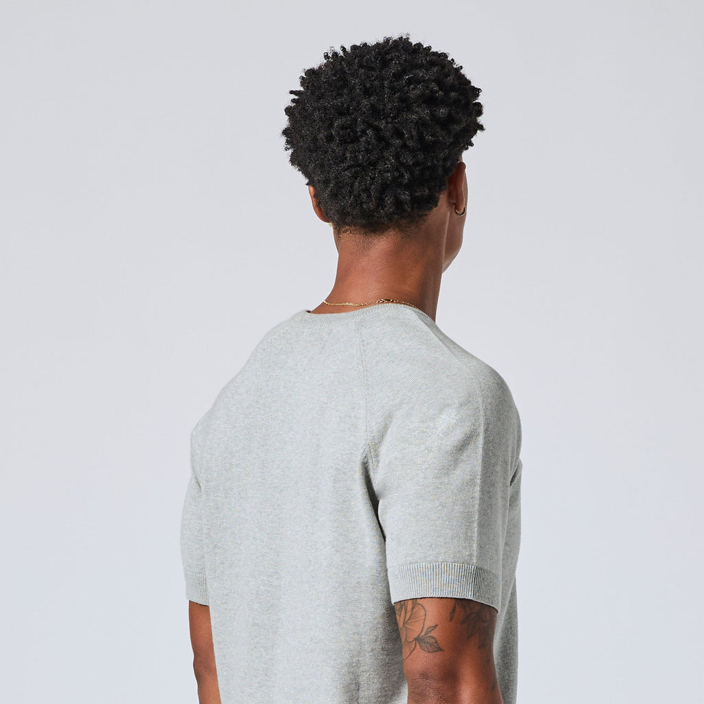 Model viewed from behind wearing a light gray short-sleeve knit t-shirt, showcasing the back collar and shoulder construction against a light gray background. Color: Heather Grey