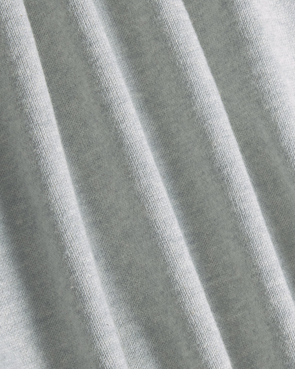 A close-up of light gray heathered fabric with soft vertical folds showing the knit texture. Color: Heather Grey