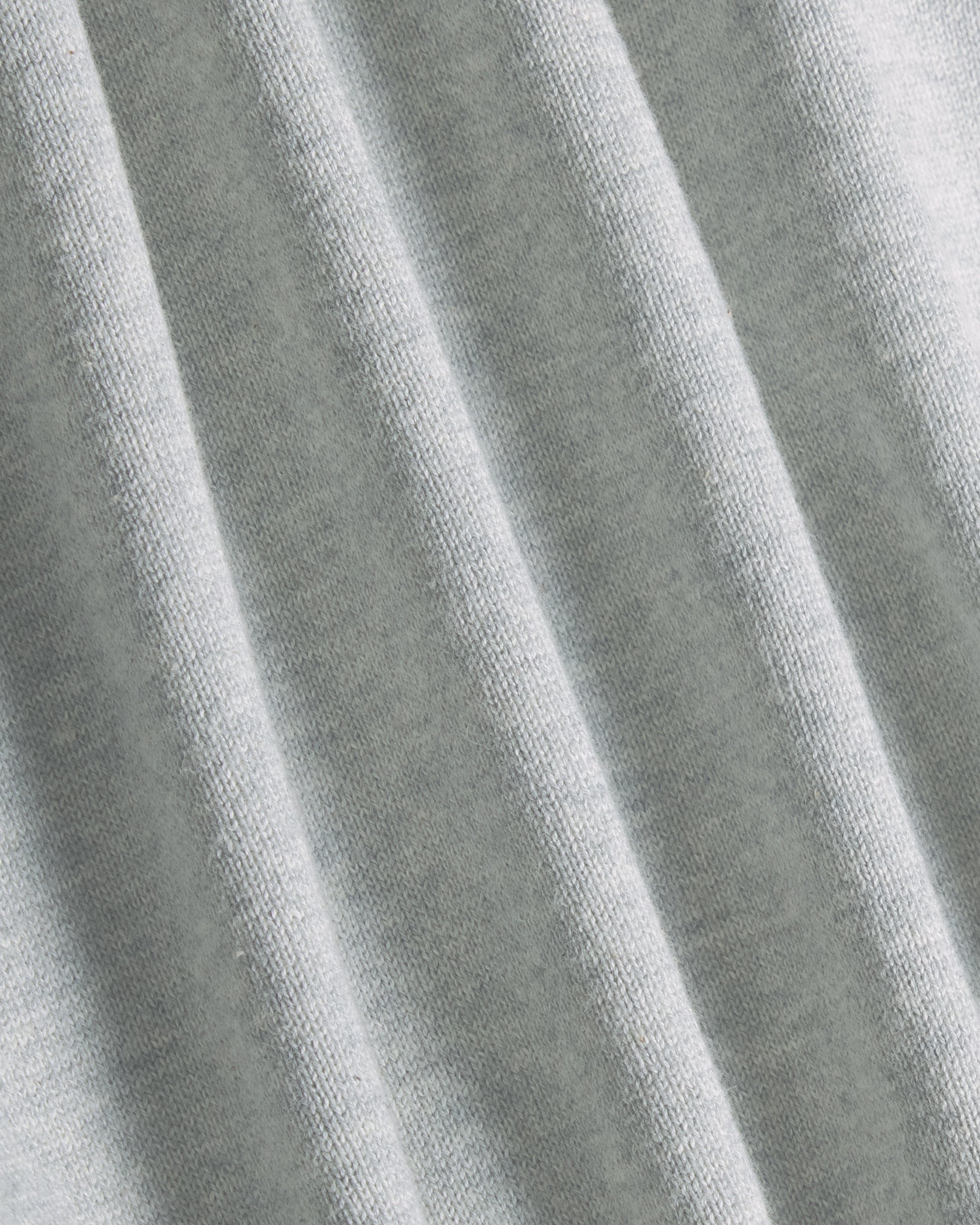 A close-up of light gray heathered fabric with soft vertical folds showing the knit texture. Color: Heather Grey