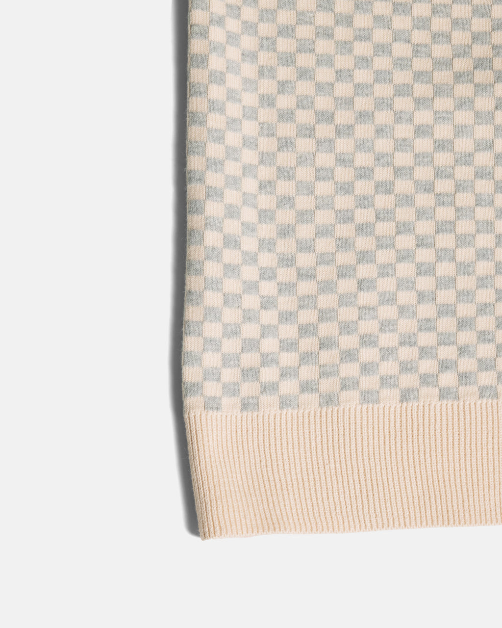 Close-up of a ribbed knit fabric with a small checkerboard pattern in light gray and cream, finished with a cream ribbed hem. Color: Saltstone Checker