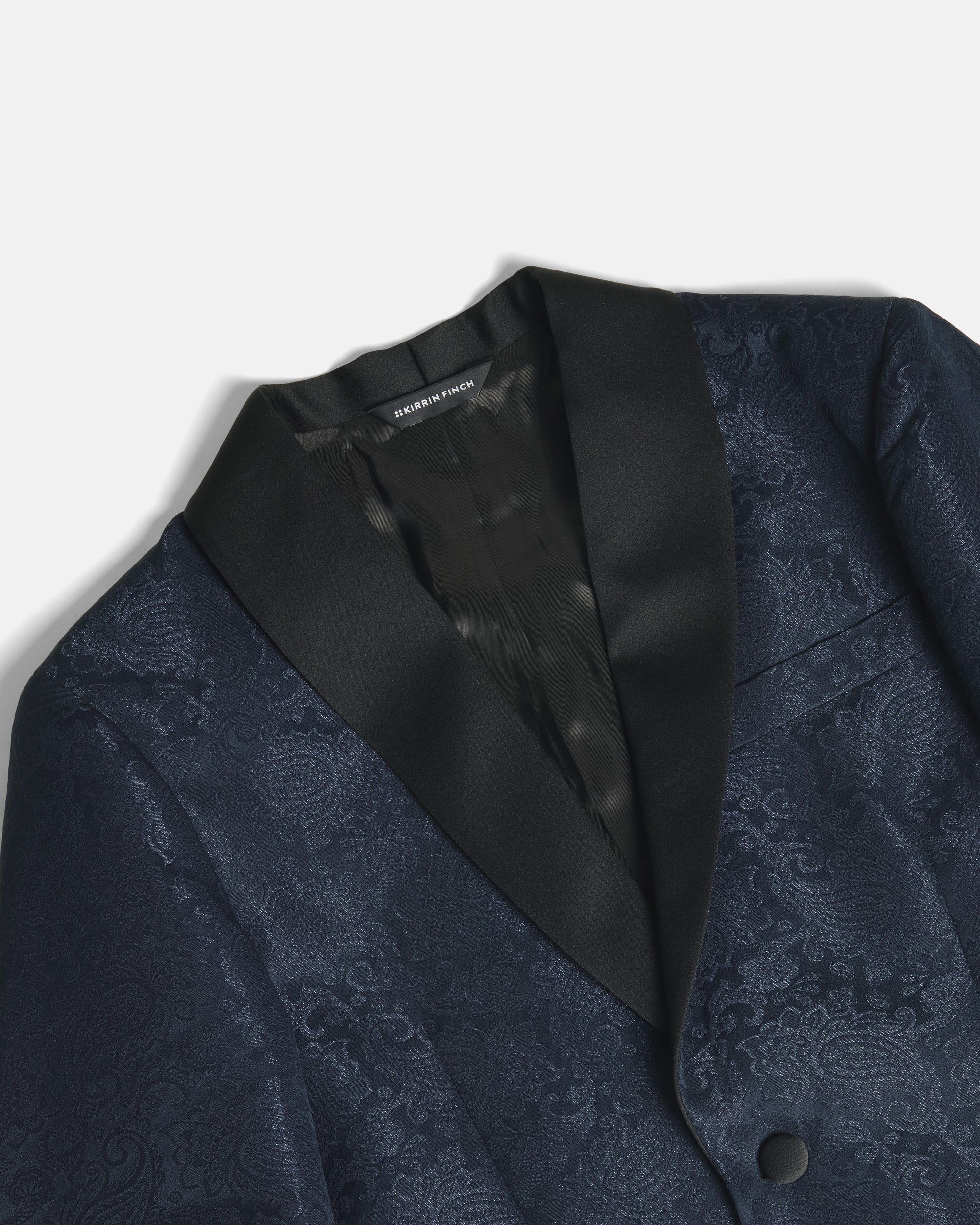 Close-up of a dark navy blue patterned suit jacket with black satin lapels, showing the interior collar label that reads Peter Millar. Color: Sapphire Brocade