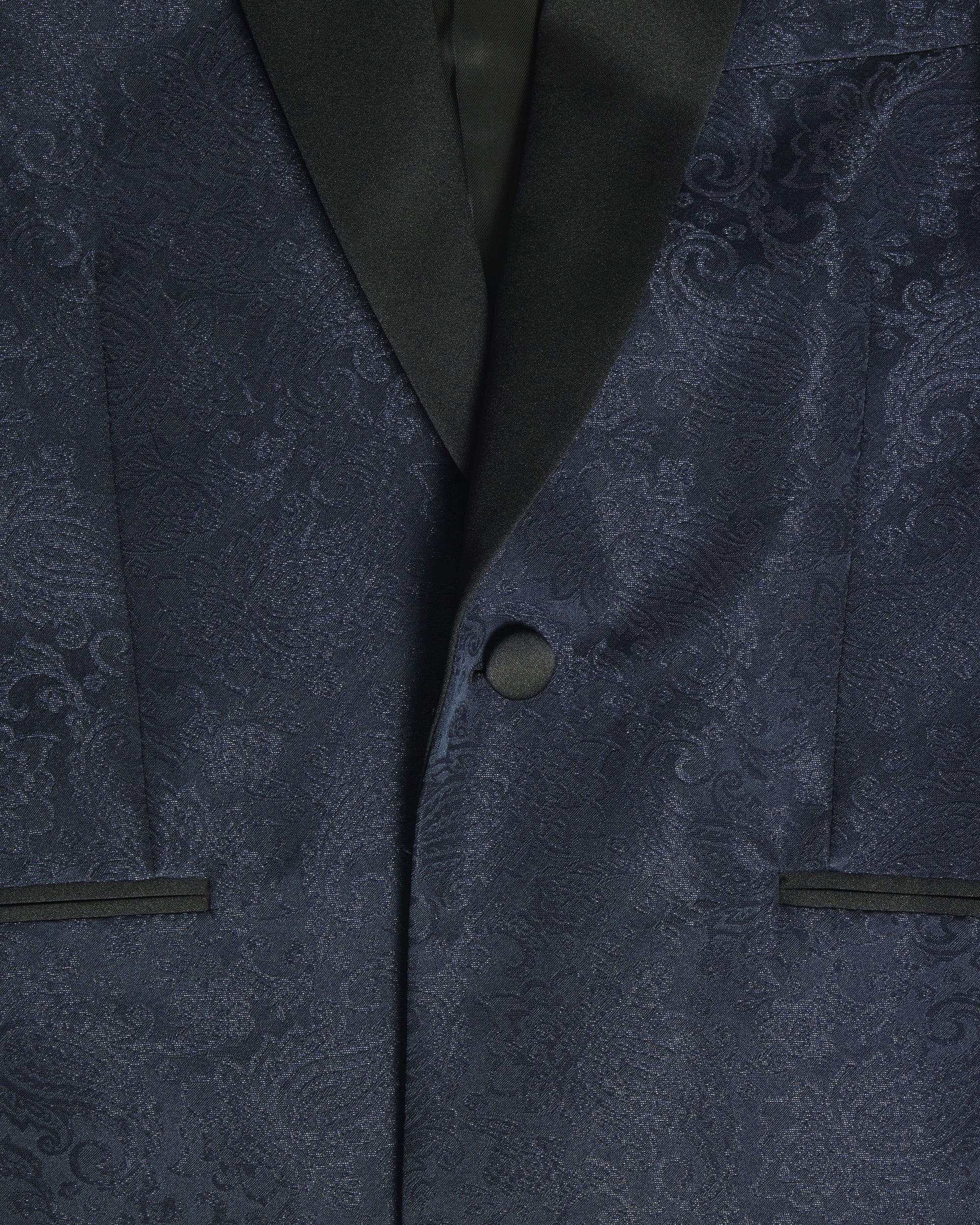 Close-up of a navy blue patterned suit jacket with black satin lapels and a matching dark button. Color: Sapphire Brocade