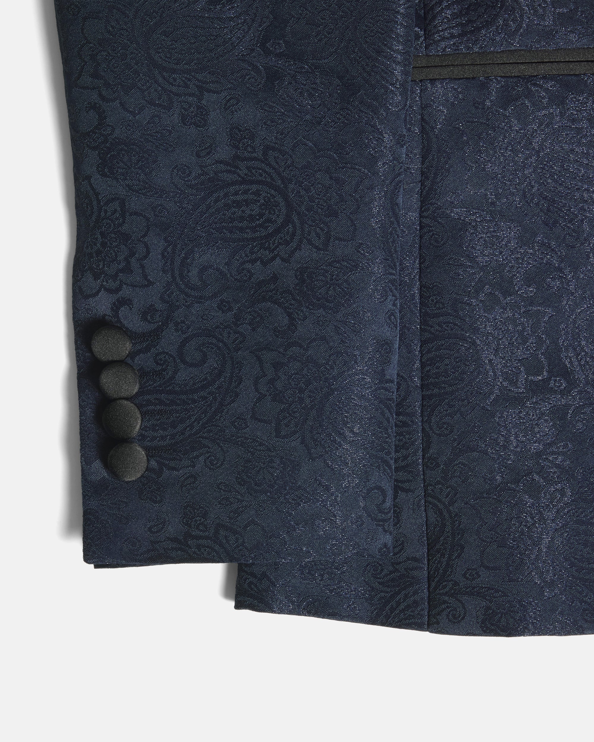 Close-up of a navy blue jacquard fabric garment, showing a detailed paisley pattern, a pocket with a dark trim, and four dark buttons on the sleeve cuff. Color: Sapphire Brocade