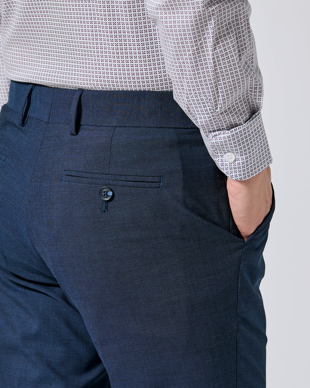 Close-up of a person wearing Atlantic blue trousers and a white shirt with a small gray grid pattern, showing the back pocket and side pocket of the trousers. Color: Atlantic Blue