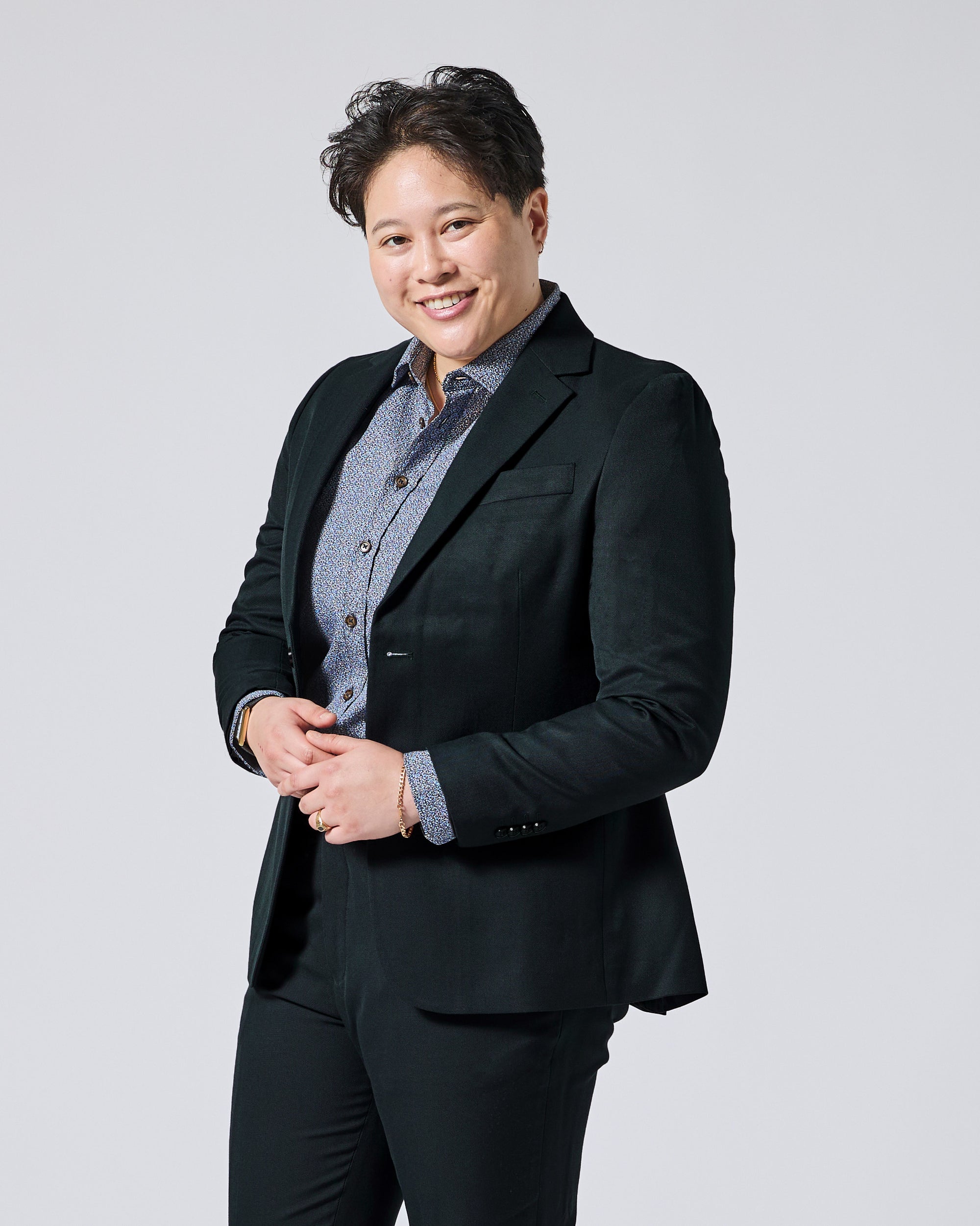 Person wearing a Phantom Green Twill Scout blazer over a blue patterned button-down shirt, paired with black trousers, standing against a solid light gray background. Color: Phantom Green Twill