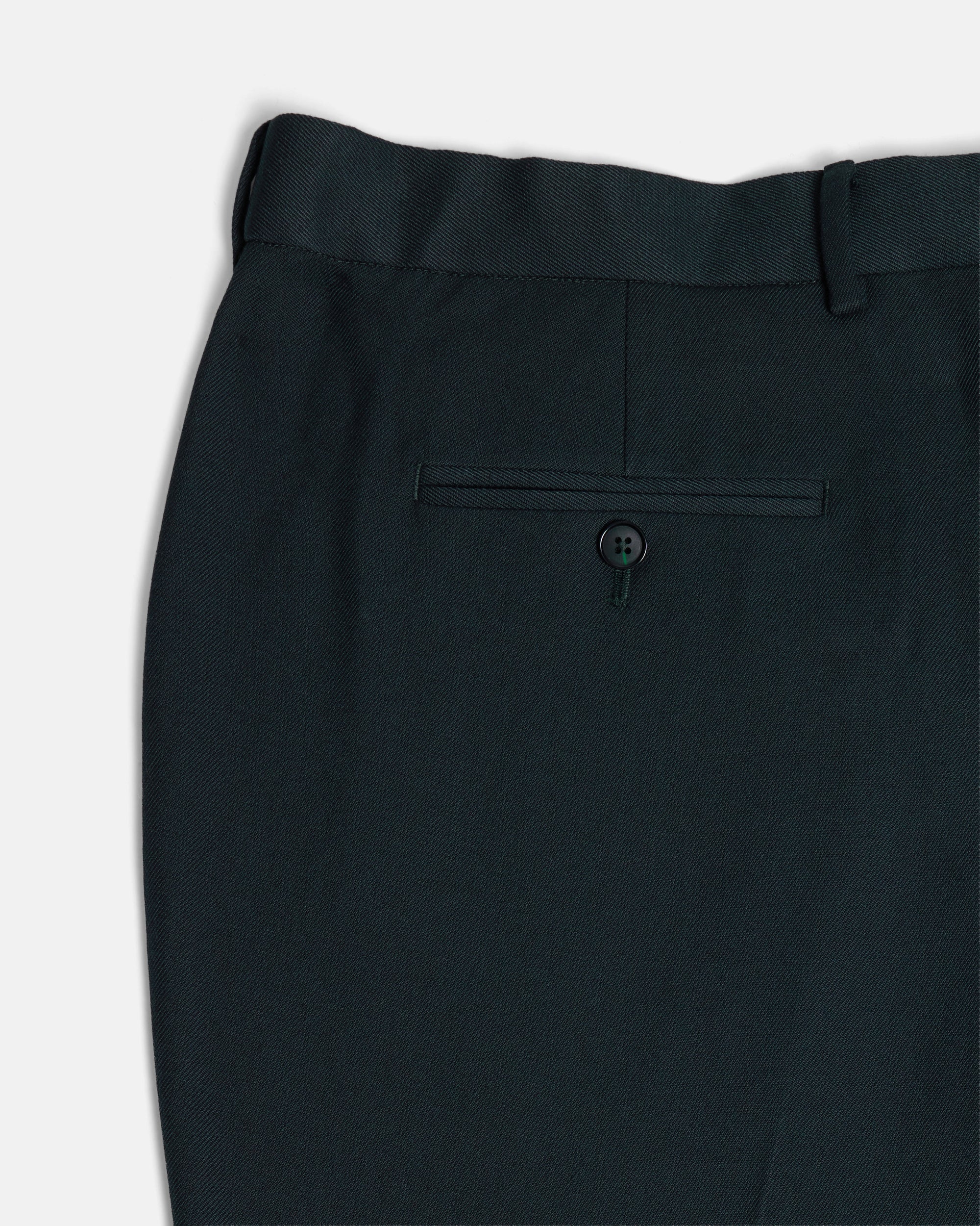 Close-up of a dark green suit pants with a button on a light gray background. Color: Phantom Green Twill