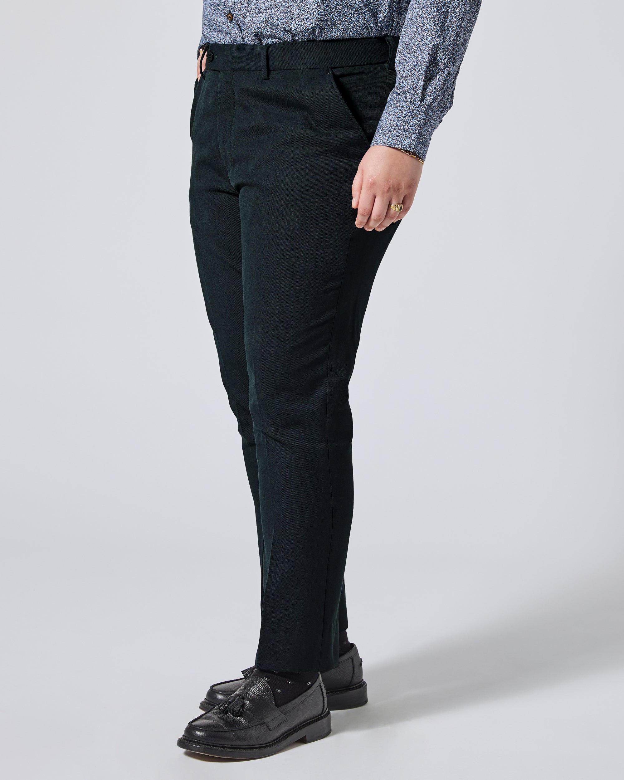 A person wearing slim phantom green scout pants with a blue patterned shirt and black loafers, shown from the waist down against a light gray studio background. Color: Phantom Green Twill