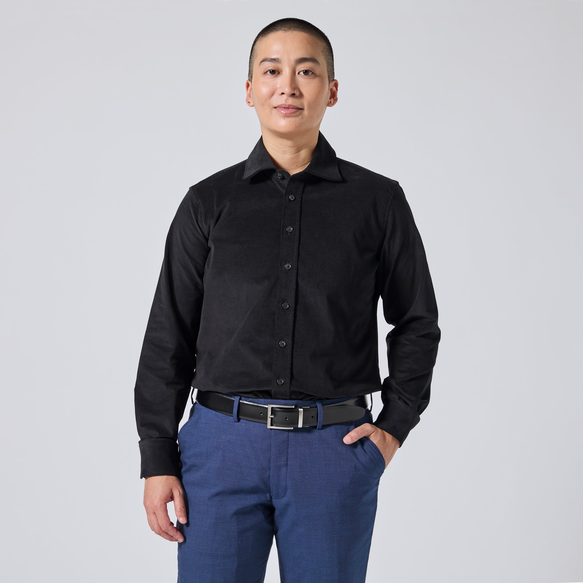 Model wearing a black long-sleeve button-down shirt and blue trousers, standing against a light gray studio background. Color: Shadow Corduroy